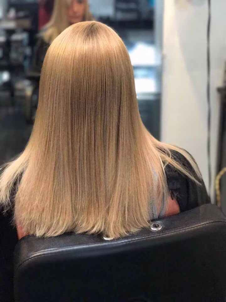 The back of a client’s freshly cut and colored blonde hair, smooth and even at the shoulders