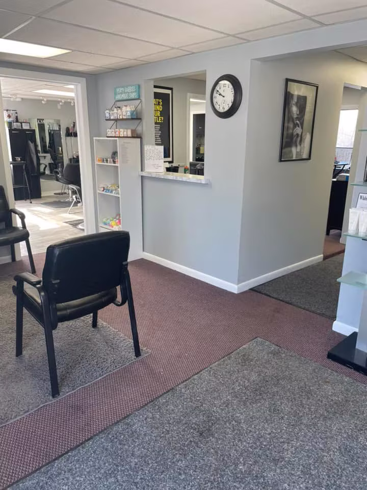The entry and front desk: a black waiting chair, a wall clock and a doorway through to the styling floor