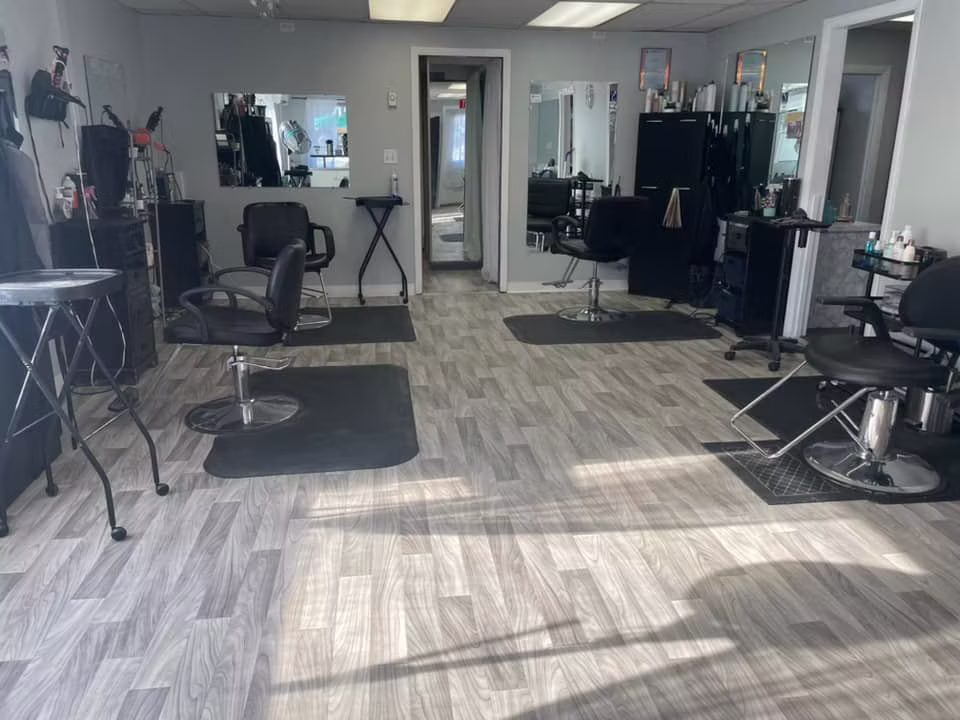The salon floor at First Impressions: black styling chairs and mirrors on gray plank flooring, with sunlight across the room