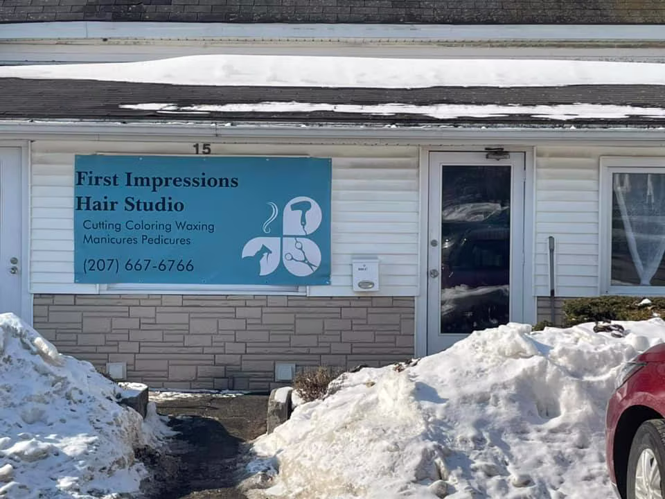 The salon’s entrance at 15 High Street: a white building with a teal First Impressions Hair Studio sign beside the door, with snowbanks out front